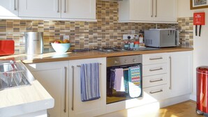 A modern kitchen with white cabinets, a tiled backsplash, a microwave, and a red trash bin. - 2 bedroom accommodation in Scarborough (Scarborough)
