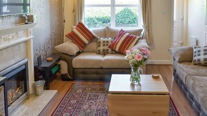 A cozy living room with a fireplace, a sofa set, a coffee table, and a view of greenery outside. - 2 bedroom accommodation in Scarborough (Scarborough)