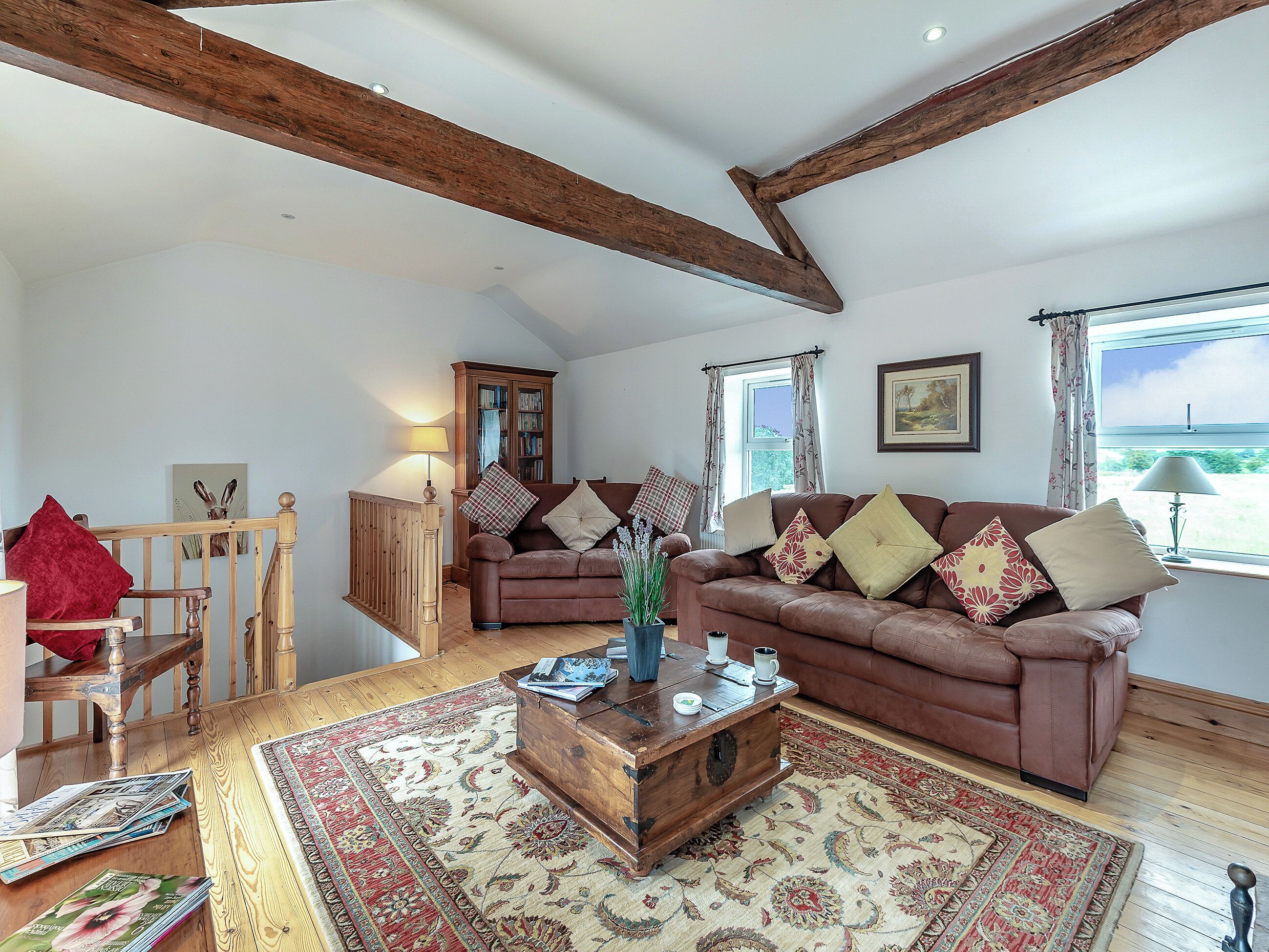 A spacious living room with a brown leather sofa, wooden coffee table, and a large rug.