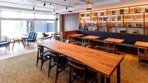 A modern meeting room with a long wooden table, blue chairs, and a sofa. There are shelves with framed pictures on the wall. - Hotel Munin Furano (Furano)