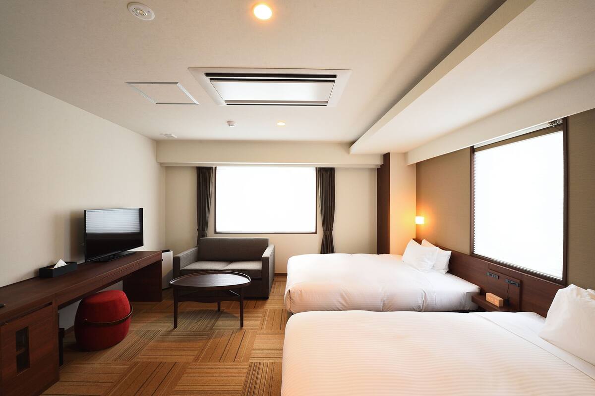 A hotel room with two beds, a TV, a desk, and a chair.