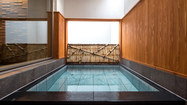 A traditional Japanese onsen with a wooden interior, a bamboo fence, and a tiled floor. - Hotel Munin Furano (Furano)