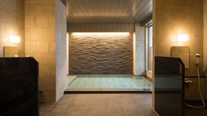 A modern bathroom with a tiled floor, a stone wall with a textured pattern, and a glass partition. - Hotel Munin Furano (Furano)