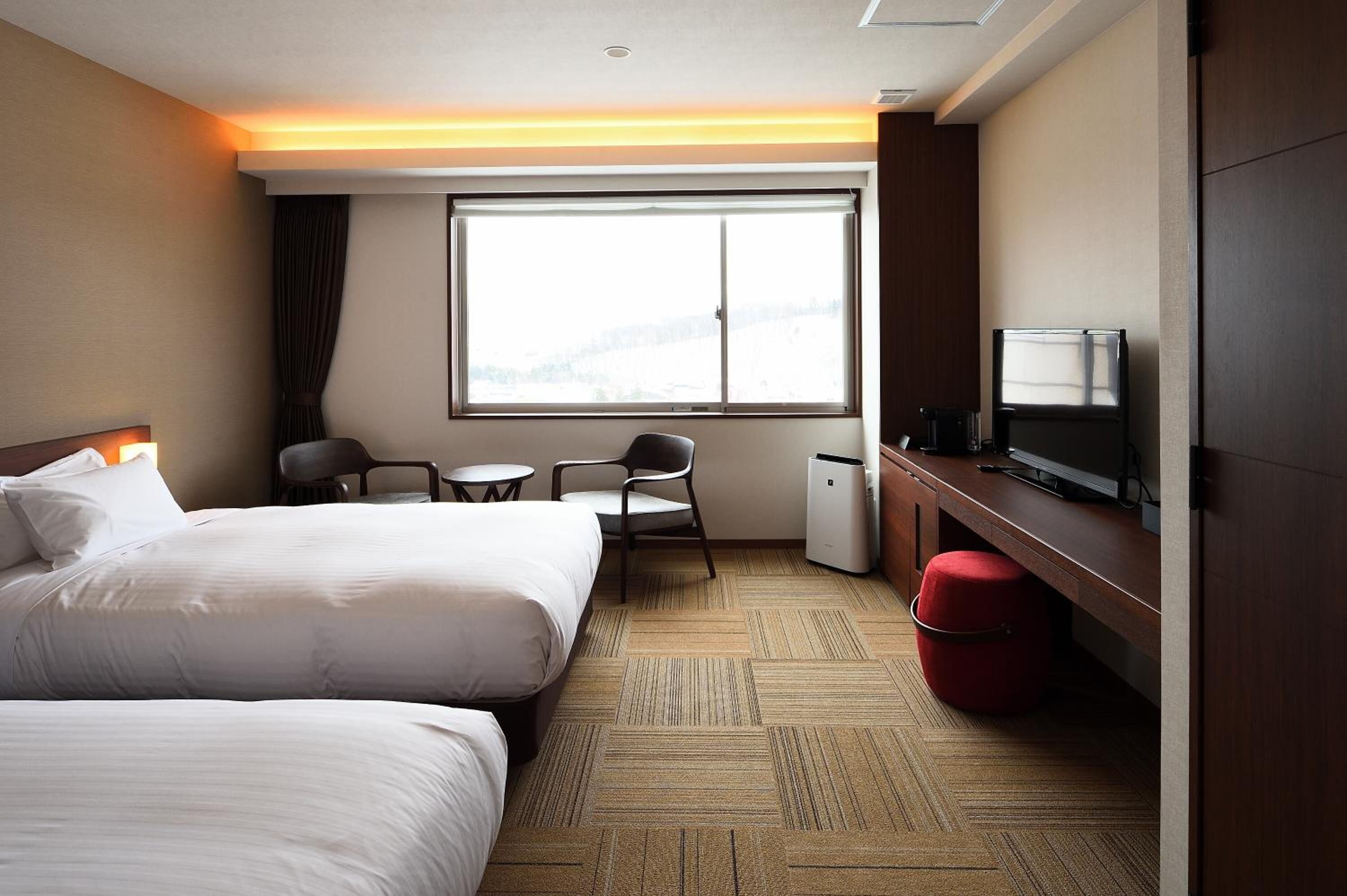 Een hotelkamer met twee bedden, een bureau met een televisie, een stoel, een klein tafeltje en een raam met uitzicht.