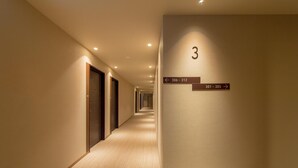 A hotel hallway with a carpeted floor, doors on the left, and a sign indicating room numbers 306-312 and 301-305 on the right. - Hotel Munin Furano (Furano)