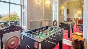 Una stanza con due tavoli da calcio, un pianoforte e una vista panoramica attraverso ampie finestre.