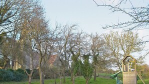 Une aire de jeux avec un toboggan et un mur d’escalade, entourée d’arbres et d’herbe.