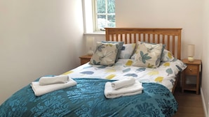 Un lit bien fait, avec une couette et des oreillers à motifs floraux, une tête de lit en bois et une table de chevet avec une lampe.