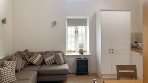 Un salon chaleureux avec un canapé, une petite table sur laquelle est posé un vase, une fenêtre avec des rideaux, une armoire blanche et une chaise en bois.