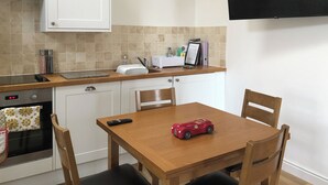 Une cuisine avec des meubles blancs, un plan de travail en bois, un four encastré et une table à manger avec des chaises.