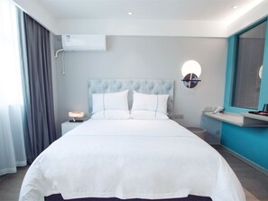 A hotel room with a large bed, a bedside table with a lamp, a wall-mounted air conditioner, and a window with curtains.