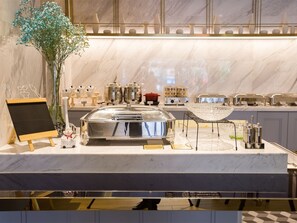 A buffet setup with a chalkboard menu, a glass bowl, and various food containers on a marble countertop.