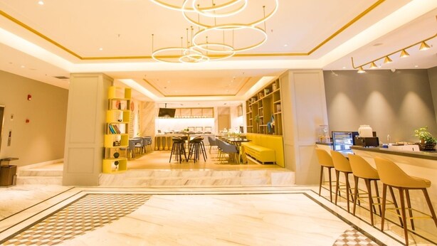 A modern hotel lobby with a central dining area, bar, and seating. - Magnotel Hotel –South Railway Station, Huizhou (Huizhou)