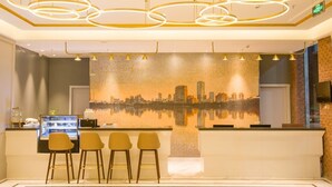 A modern reception area with a cityscape mural, a reception desk, and three bar stools. - Magnotel Hotel –South Railway Station, Huizhou (Huizhou)