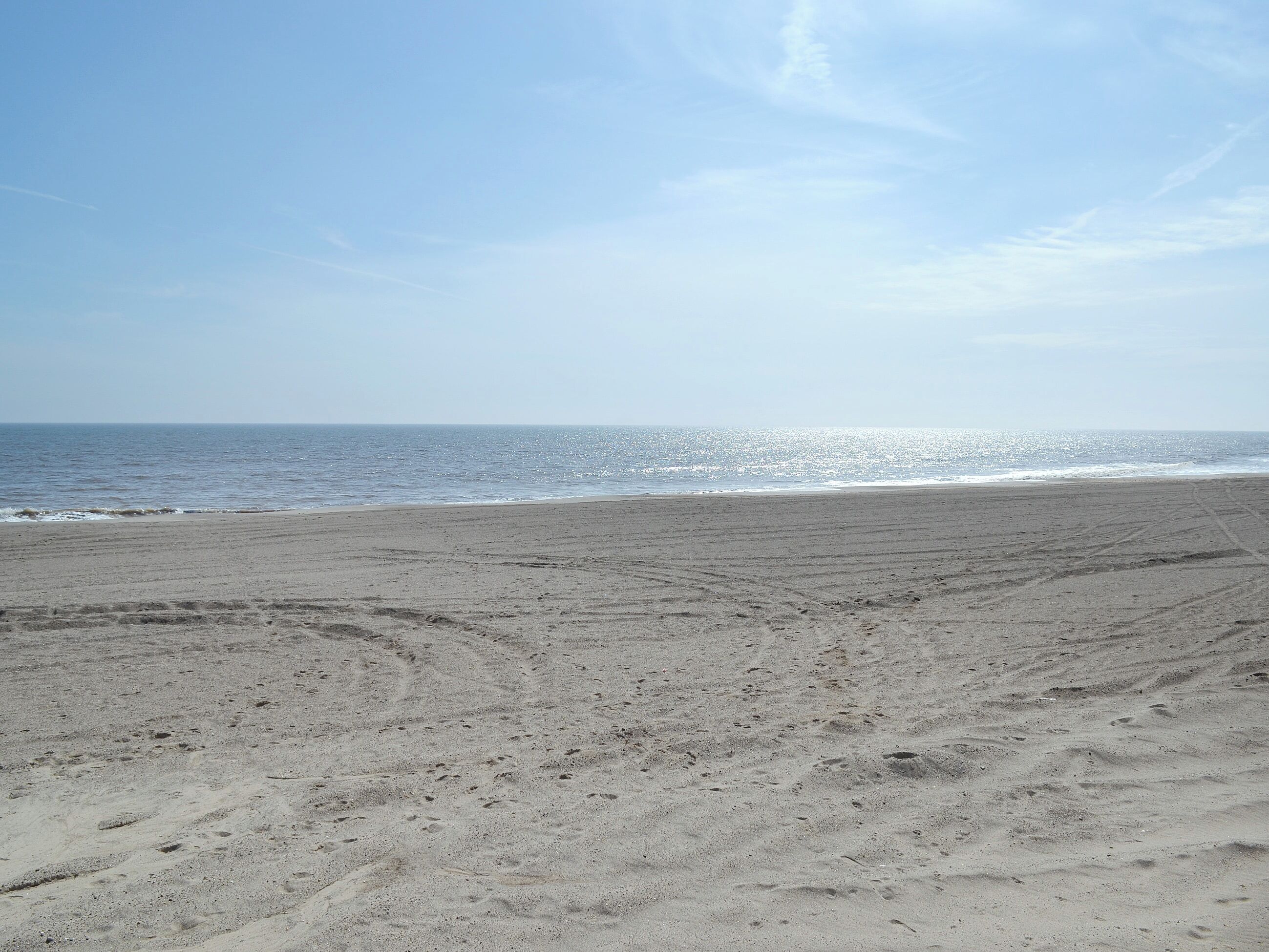 Ampia spiaggia sabbiosa con impronte che conducono all'acqua, sotto un cielo sereno.