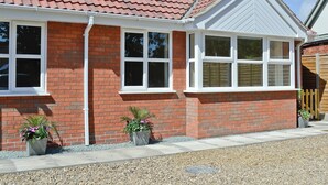 A brick house with a red tiled roof, white-framed windows, and a small garden with two potted plants.