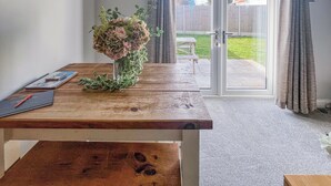 A room with a wooden table, a vase with flowers, a notebook, and a pen. There is a sliding glass door leading to a backyard with a picnic table.