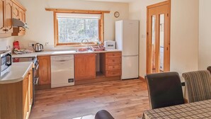 Une cuisine compacte avec des meubles en bois, un lave-vaisselle, un réfrigérateur et une fenêtre donnant sur les arbres.