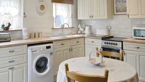 Cocina compacta con lavadora, lavamanos, estufa y microondas. Hay una mesa con una silla y un cuenco decorativo.