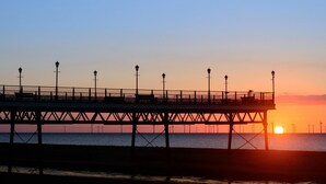 Un muelle que se adentra en el agua, con un atardecer de fondo.