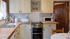 Cocina compacta con armarios blancos, microondas, tostadora, hervidor y pileta.