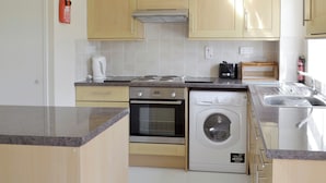 Una cocina compacta con armarios de madera, horno empotrado, lavadora y un lavamanos de acero inoxidable.