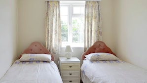 Un dormitorio con dos camas individuales, una mesita de noche, una lámpara y una ventana con cortinas de flores.