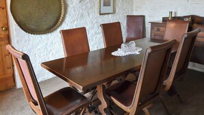 Un coin repas avec une table en bois et six chaises, une assiette décorative accrochée au mur et un tableau encadré au-dessus de la table.