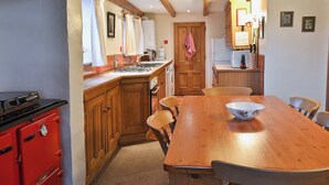 Une cuisine avec des meubles de rangement en bois, un poêle rouge, une table à manger en bois avec des chaises et un évier blanc.