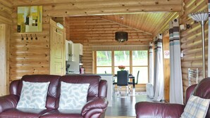 A log cabin interior with a living area featuring two leather sofas, a dining table, and a kitchen area.