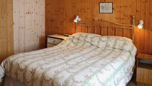 Een slaapkamer met een wand bekleed met houtpaneel, een bed met bloemenprint beddengoed, een nachtkastje, een dressoir en een ingelijste foto aan de muur.
