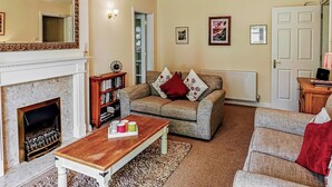 Een woonkamer met een open haard, een bank, een bijzettafeltje en een boekenkast.