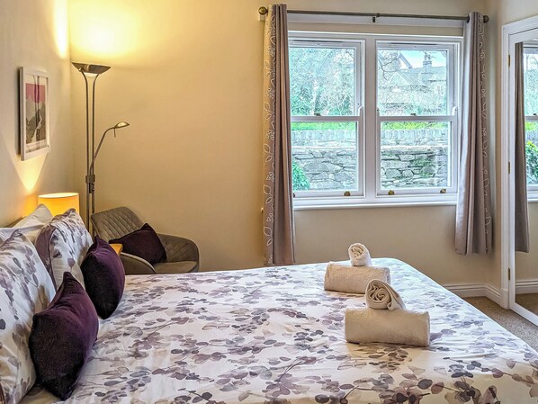 A bedroom with a bed, a chair, a lamp, a window with curtains, and a view of the outside.