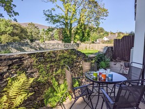 A patio with a table and chairs, a stone wall, and a view of a garden and hills.