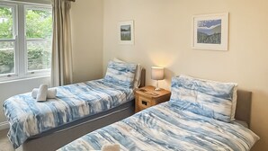 Een slaapkamer met twee bedden, een nachtkastje, een lamp en twee ingelijste foto’s aan de muur.