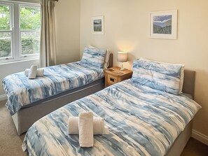 Une chambre avec deux lits, une table de chevet, une lampe et deux tableaux encadrés au mur.