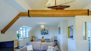 A cozy living room with a high ceiling, a wooden beam structure, a flat-screen TV, a grey sofa, and a dining area with chairs and a table. - 4 bedroom accommodation in Wells-next-the-Sea (Wells-next-the-Sea)