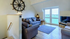 A cozy living room with a large window, a sail wheel decoration, a flat-screen TV, and a wooden floor. - 4 bedroom accommodation in Wells-next-the-Sea (Wells-next-the-Sea)