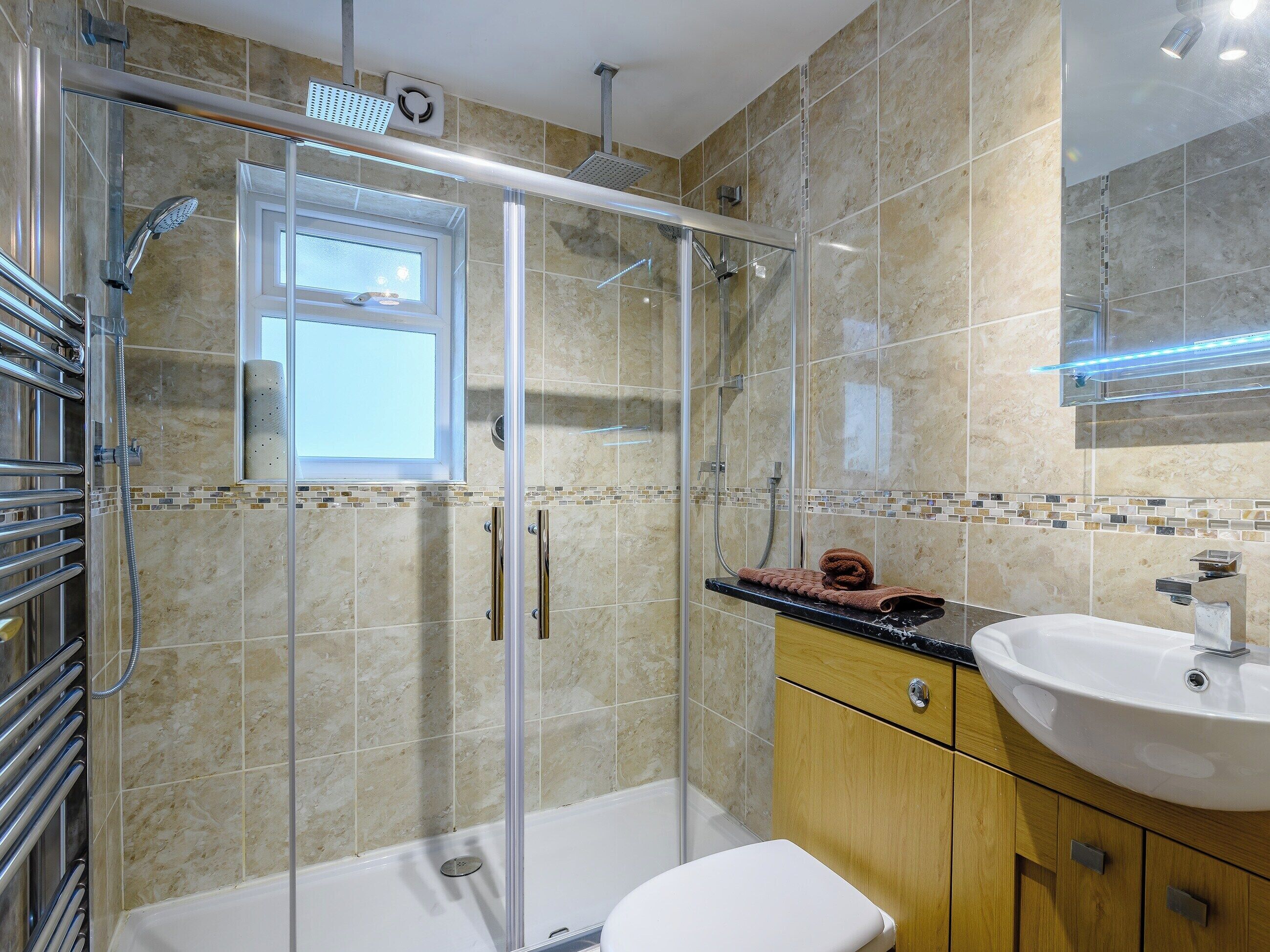 Un baño moderno con ducha envuelta en vidrio, inodoro blanco y tocador de madera con lavamanos.