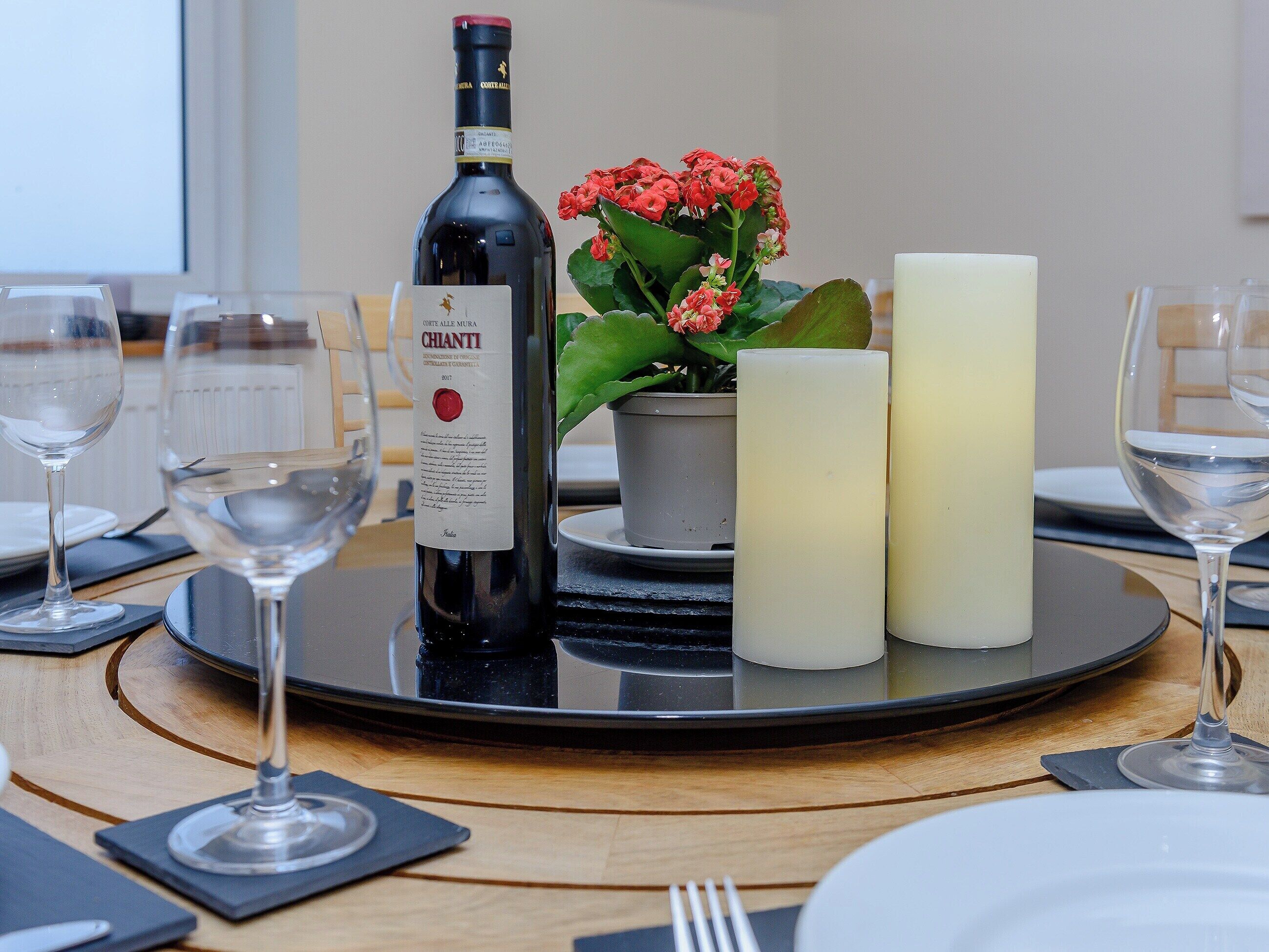 A dining table with a bottle of Chianti wine, a candle, and a potted plant.