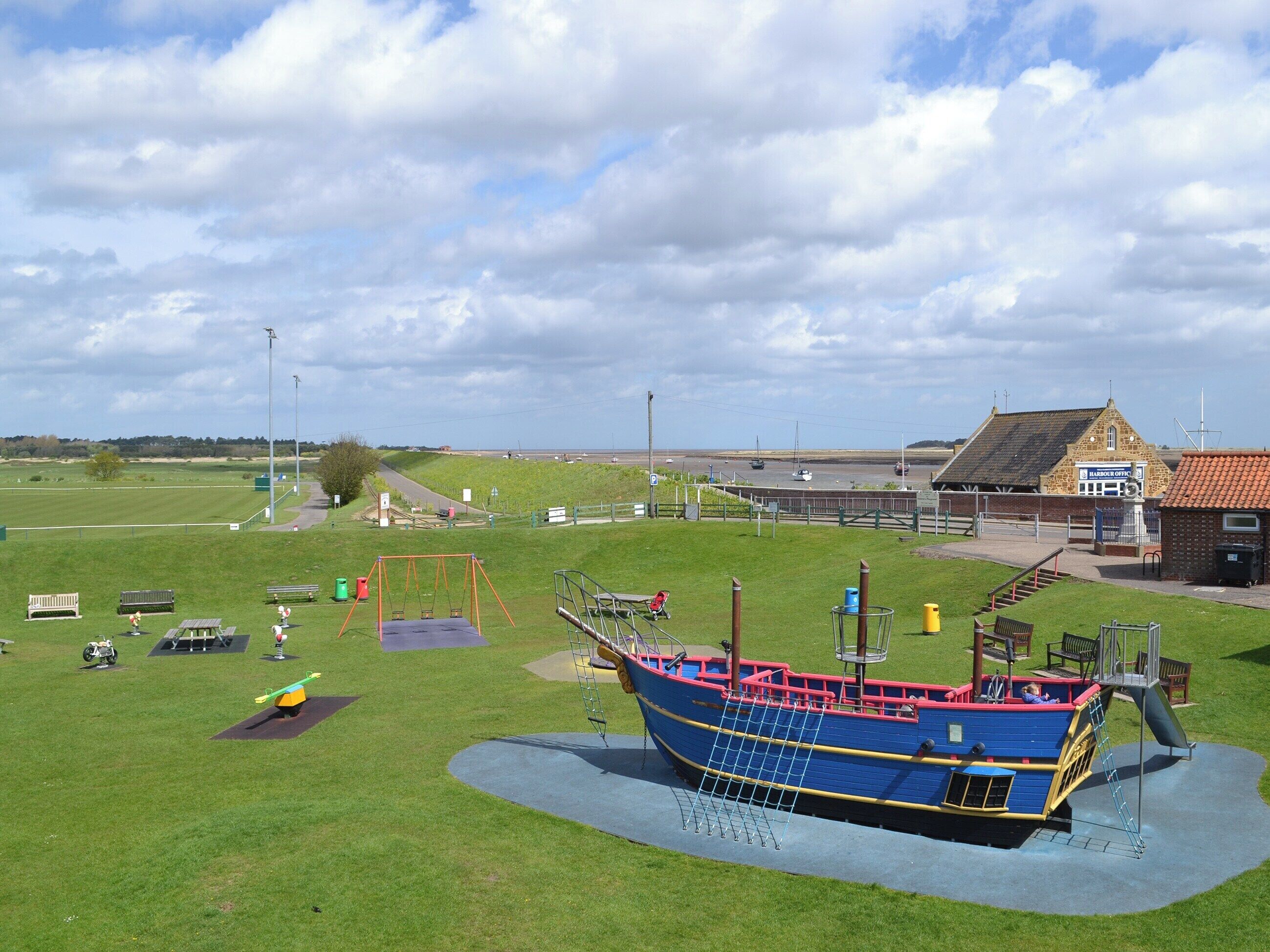 A playground with a ship-shaped play structure, a grassy field, and a building labeled "Harbor Office" in the background.