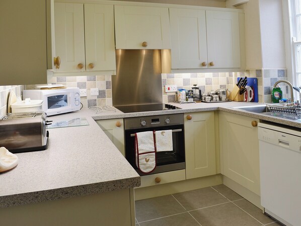 A compact kitchen with white cabinets, a stainless steel range hood, a microwave, a toaster, and a dishwasher.