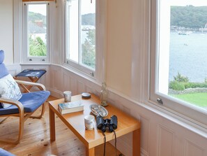 A room with a wooden table, a chair, a camera, and a view of a body of water through large windows. - 2 bedroom accommodation in Fowey (Fowey)