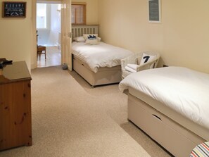 A bedroom with two beds, a wooden dresser, and a wicker chair.