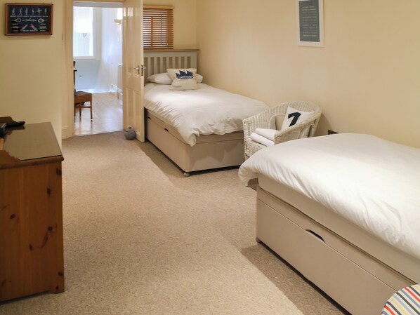 A bedroom with two beds, a wooden dresser, and a wicker chair.