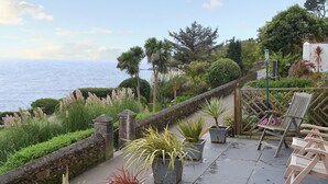 A patio with potted plants, a wooden chair, and a view of the sea.