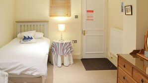 A bedroom with a bed, bedside table, lamp, dresser, and a door with a fire safety sign.