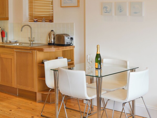 A modern kitchen with a glass table, white chairs, a toaster, and a bottle of champagne.