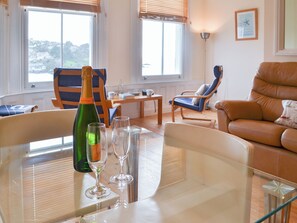 A living room with a glass table, a bottle of champagne, and two glasses. There are two chairs, a sofa, and a lamp. - 2 bedroom accommodation in Fowey (Fowey)