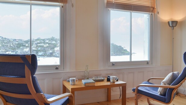 A room with two windows, a wooden table with a mug, a chair, and a lamp.
